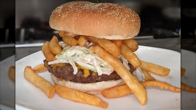 Cheeseburger topped with french fries and coleslaw on white plate.