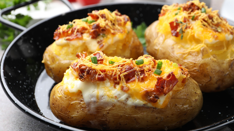 Three loaded baked potatoes in a dish, topped with sour cream, cheese, chives, and bacon