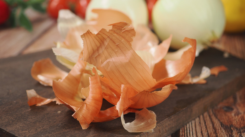 Onion peels in front of onions and other vegetables on a cutting board