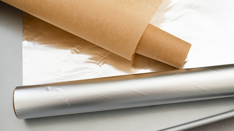 A roll of parchment paper over a roll of aluminum foil both sitting on a baking sheet