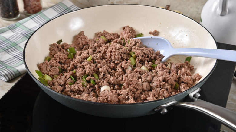 Ground beef cooking in a pan with green onions