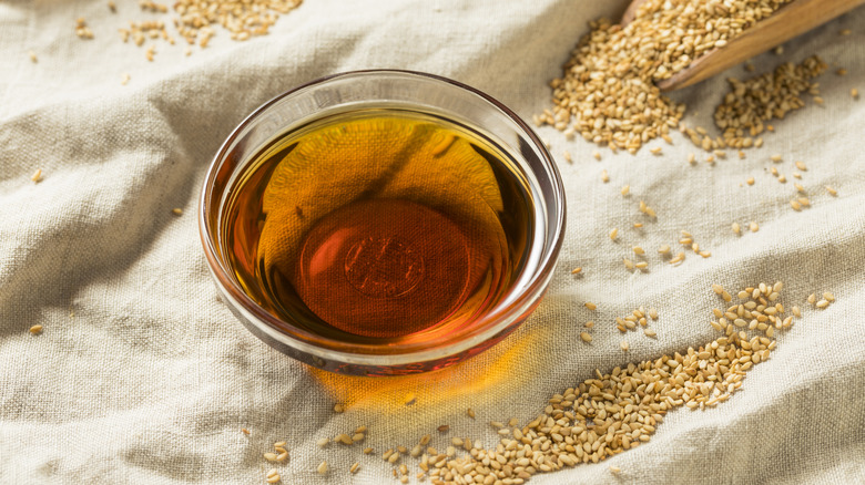 Sesame oil in small bowl surrounded by sesame seeds
