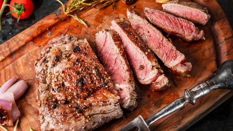 A perfectly seasoned, medium-rare ribeye steak on a wooden cutting board.