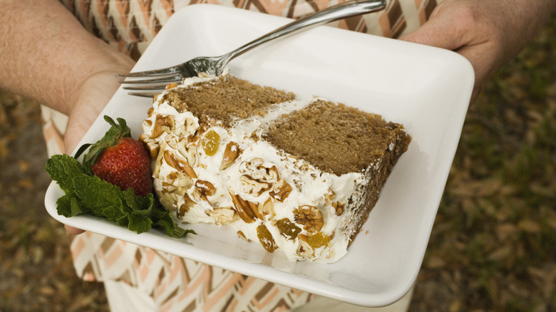A close up of a slice of Lady Baltimore Cake with strawberry garnish, held on a white plate