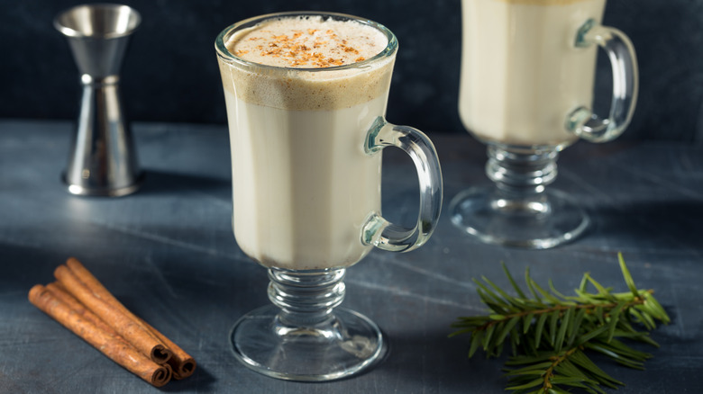 Tom and Jerry cocktail with cinnamon sticks and sprigs of herb