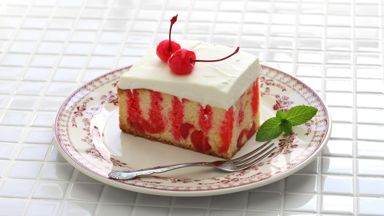 slice of Jello poke cake topped with two cherries on a plate with a fork and sprig of mint on the side