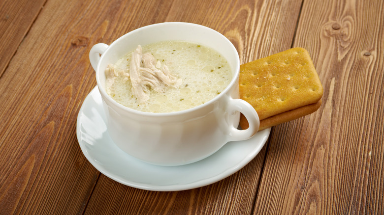 A mug of chicken mull served with some saltine crackers