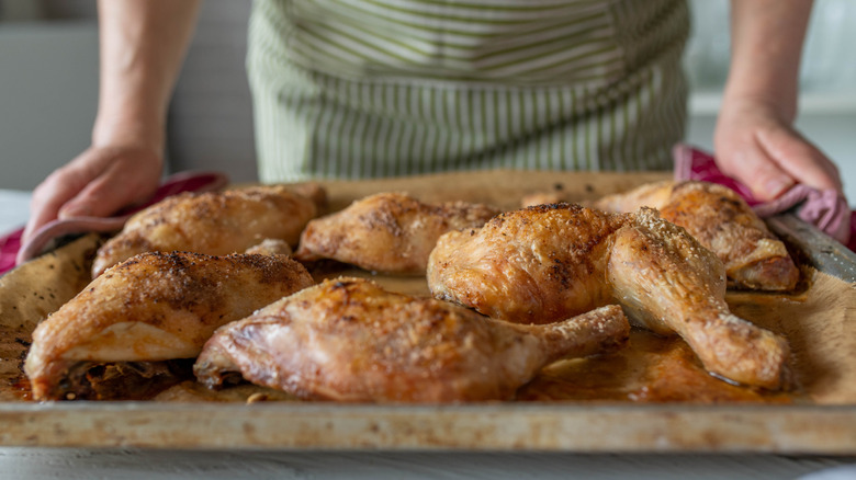 A person serving pieces of baked chicken on a tray