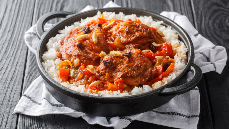 A pot filled with Country Captain chicken with white rice on top of a striped towel
