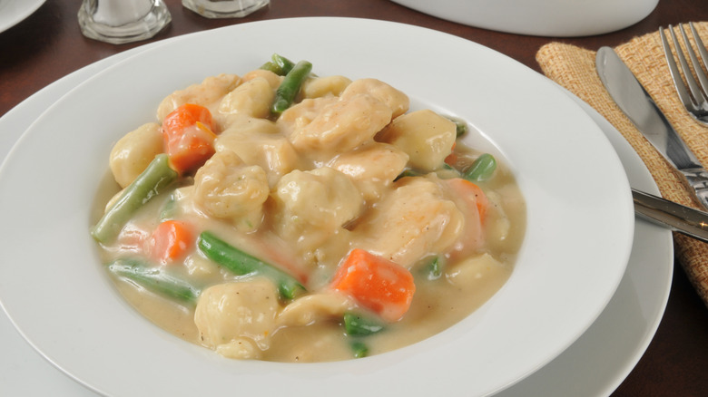 A bowl of chicken and dumpling stew with carrots and green beans