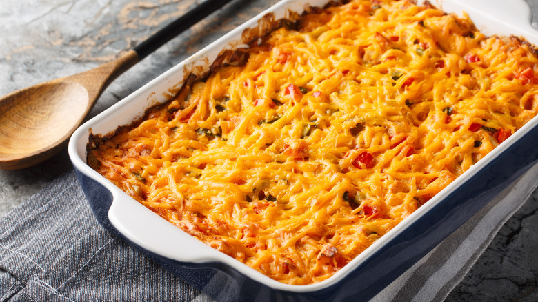 A casserole dish filled with King Ranch chicken next to a wooden spoon
