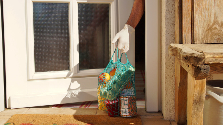 Hand grabbing groceries on the porch from behind the door