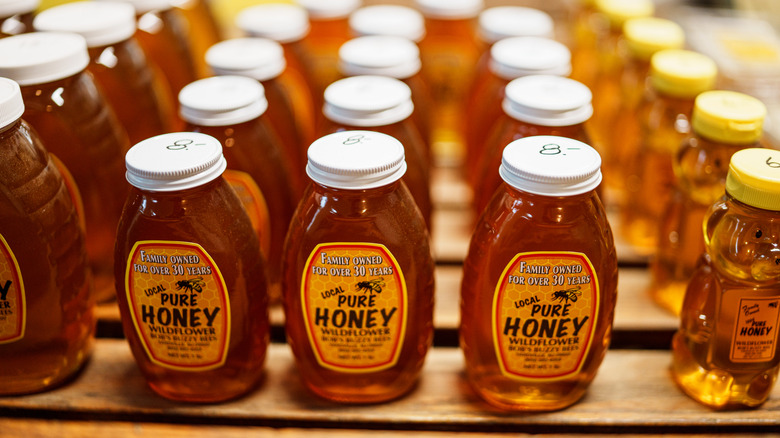 Jars of honey lined up on a wooden shelf