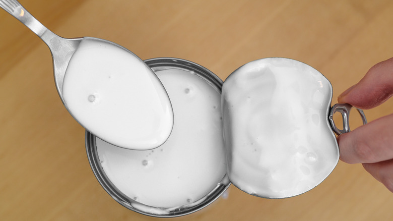 Top view of a can of creamy white coconut milk with spoon