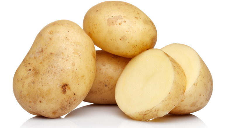 Whole and sliced potatoes on white background