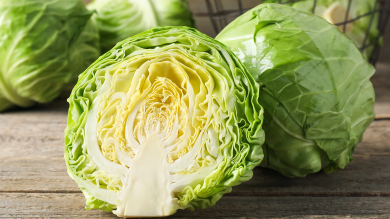 Half of a green cabbage in front of other whole cabbages on wooden surface.