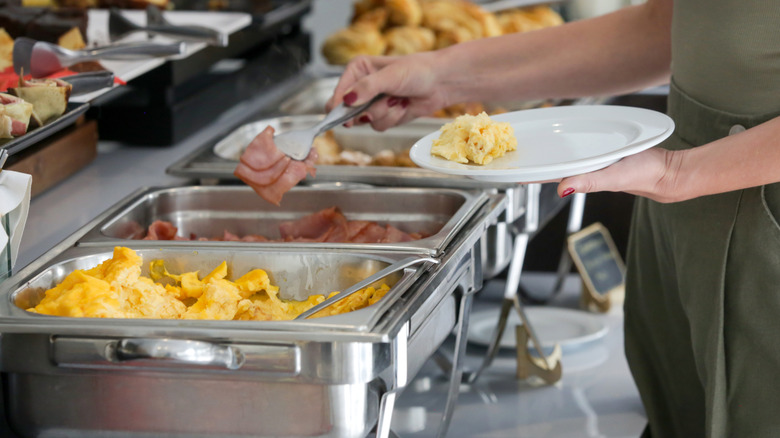 Hands taking eggs and ham from buffet line