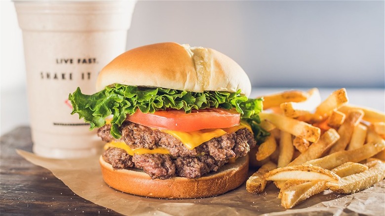 A double cheeseburger and french fries in front of a shake