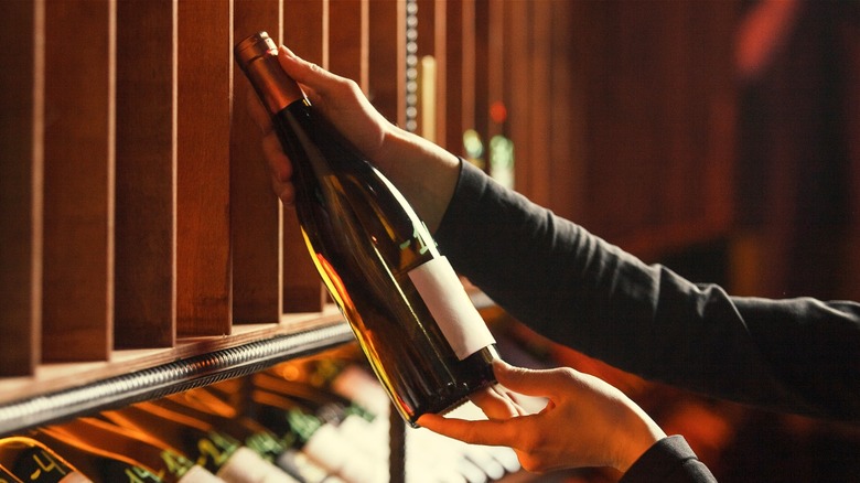 An amber-colored bottle of wine being selected from a rack.