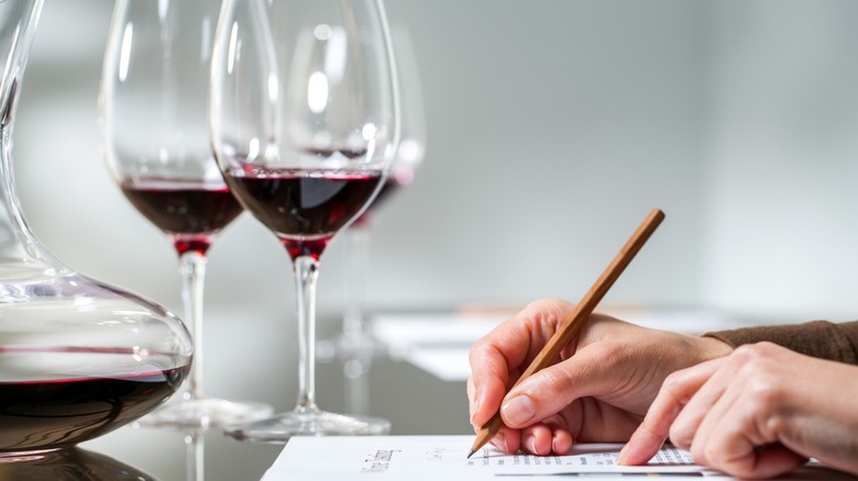 Tasting notes being written for glasses of red wine.