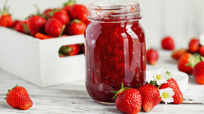 A jar of strawberry jam next to fresh strawberries