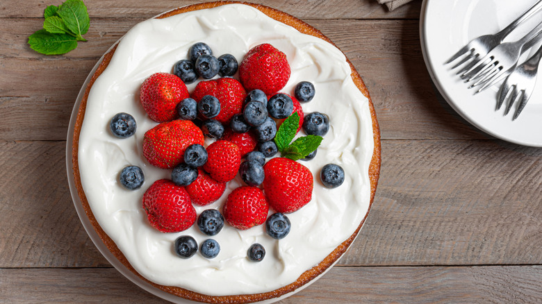 A cake topped with fresh blueberries, strawberries, and mint