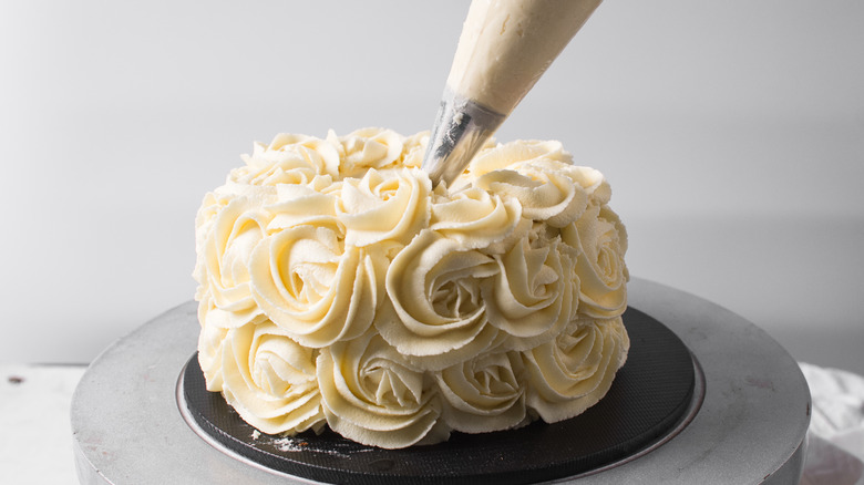 A person piping rosettes onto a cake