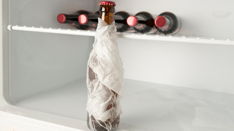 Bottle wrapped in a wet paper towel in front of a freezer shelf with unwrapped bottles in the background.