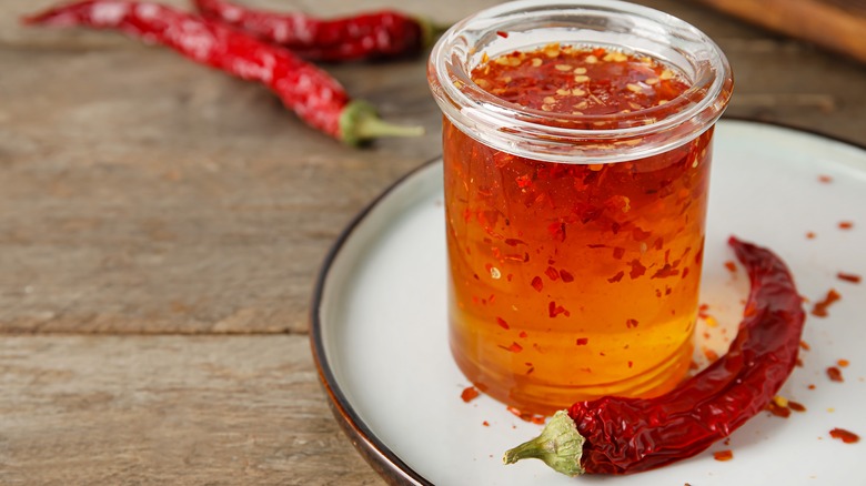 A jar of chili infused honey on a white plate on a wood surface