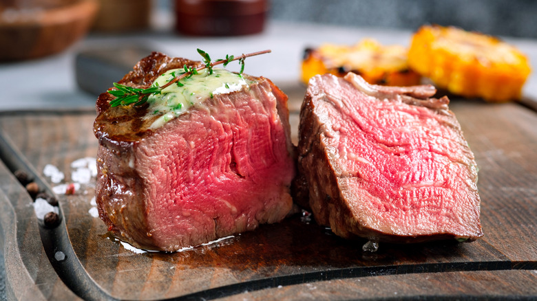 halved filet mignon steak on a wooden cutting board topped with herby butter