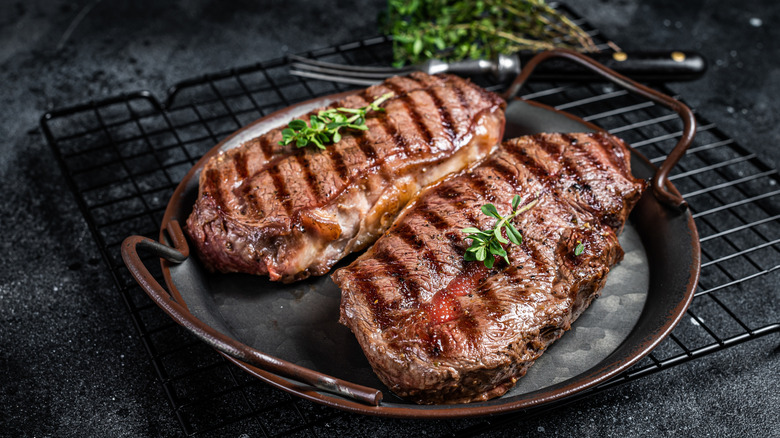 two grilled flat iron steaks in a cast iron dish topped with herbs
