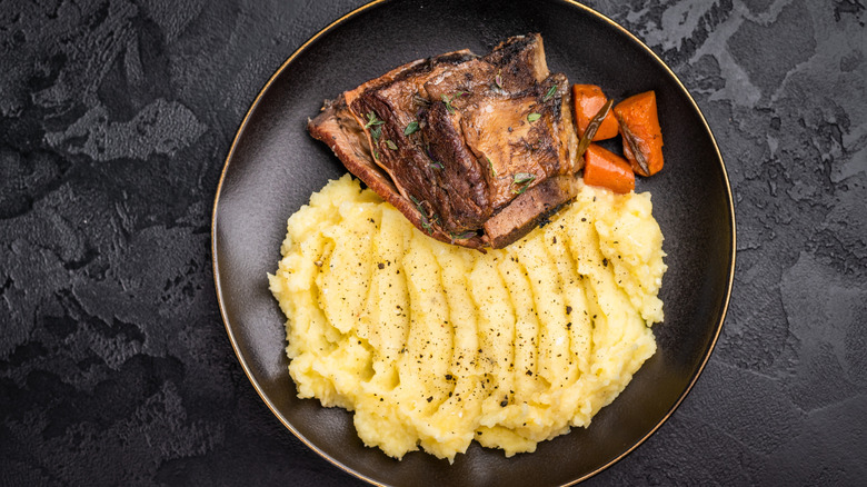 braised beef short ribs on a black plate with mashed potatoes and roasted carrots