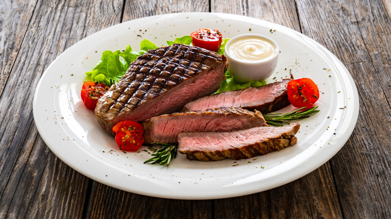 grilled sirloin steak on a white ceramic plate surrounded by vegetables