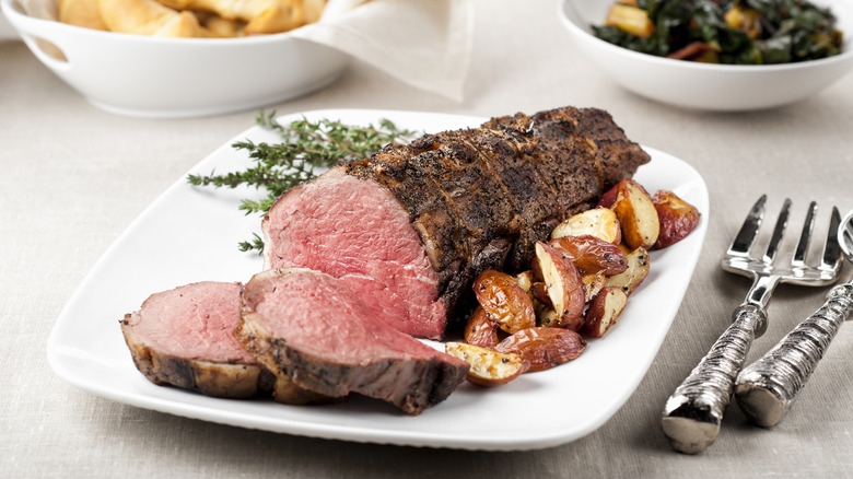sliced roasted beef tenderloin on a white plate with roasted potatoes