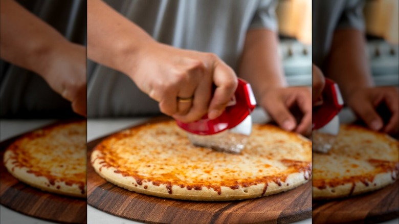 Cheese pizza being sliced on a wooden cutting board