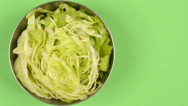 Shredded iceberg lettuce in a metal bowl on a bright green background