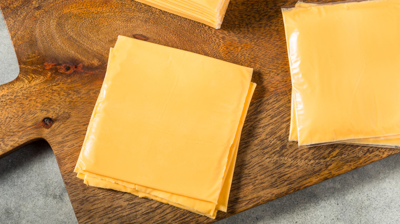 American cheese slices stacked on a wooden cheese board