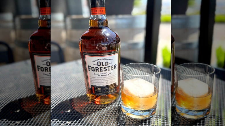 bottle of Old Forester 100 Proof on a table next to a glass of bourbon on the rocks