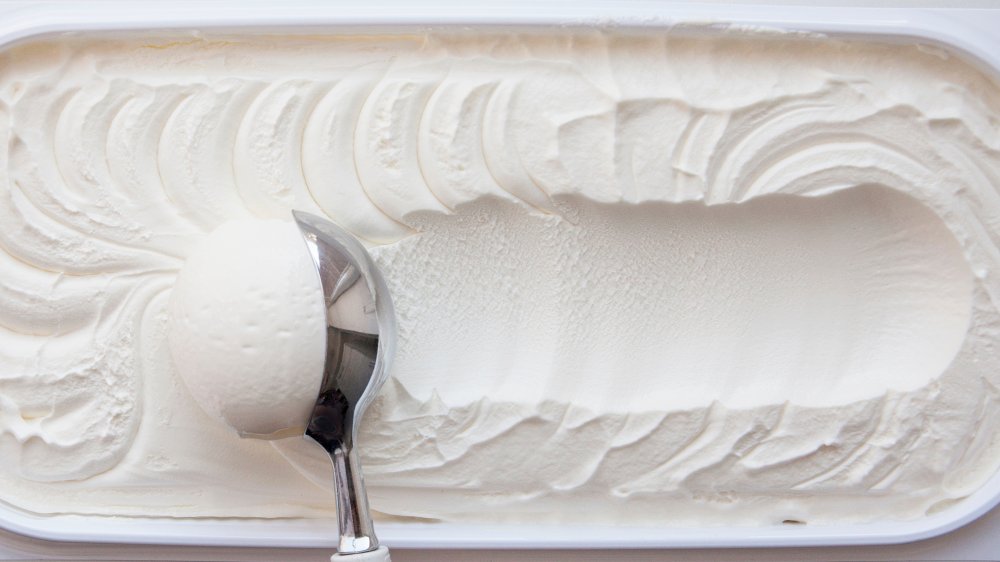 carton of vanilla ice cream with a scoop dragging across the top