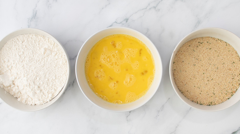 eggs, flour, and breadcrumbs in white bowls