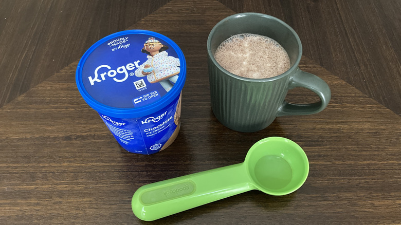 Mug of hot chocolate with a carton of ice cream and a scoop