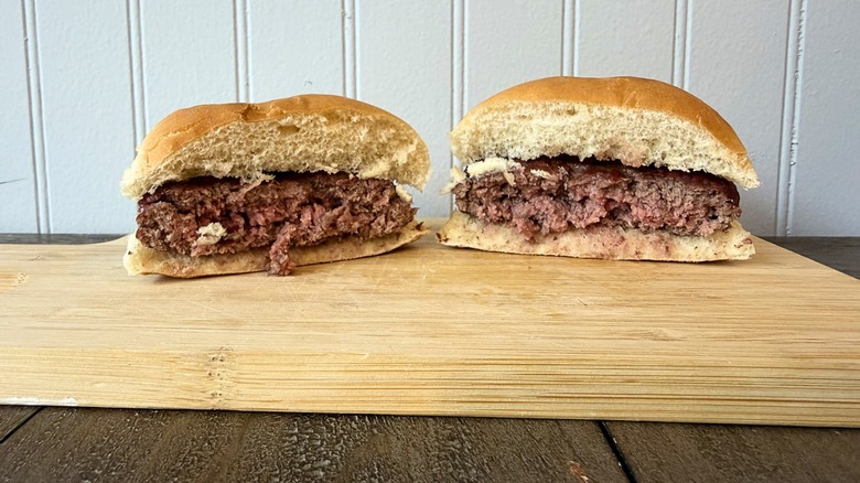 A close-up of a burger cut in half on a wooden cutting board, showing a juicy, pink middle