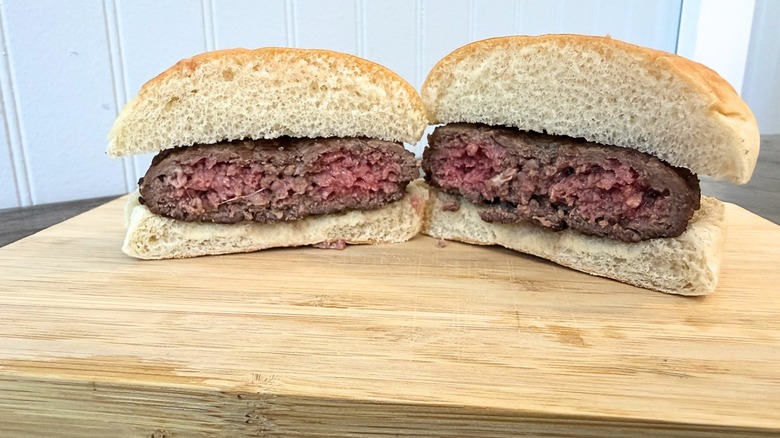 A close-up of a burger cut in half on a wooden cutting board, showing a lightly pink and juicy center