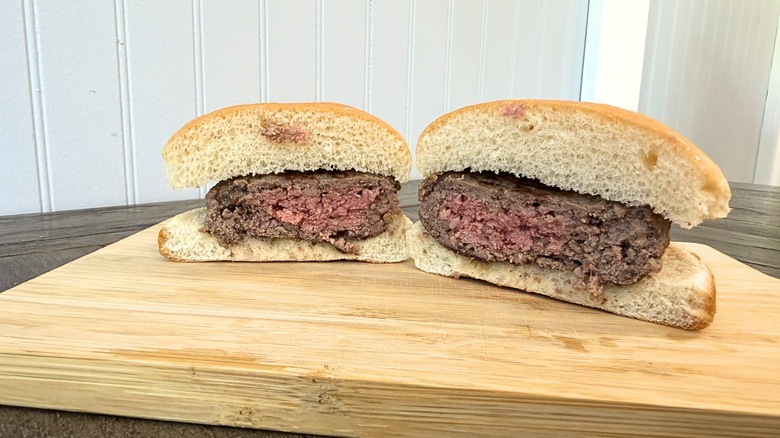 A close-up of a burger cut in half on a wooden cutting board, showing a pink center and a brown exterior