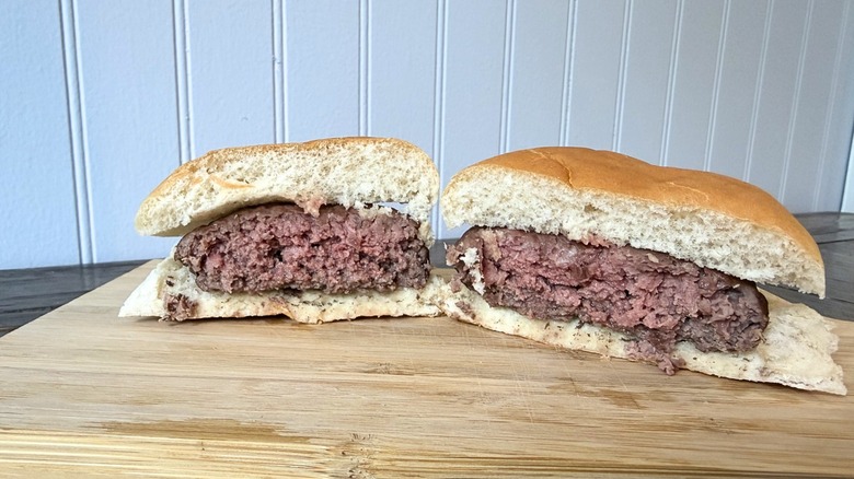 A close-up of a burger cut in half on a wooden cutting board, showing a consistent light pink interior throughout the burger