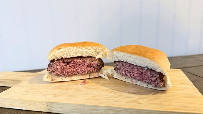 A close-up of a burger cut in half on a wooden cutting board, showing an interior that is pink throughout