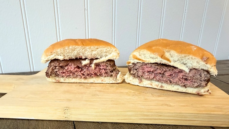 A close-up of a burger cut in half on a wooden cutting board, showing a juicy, pink center