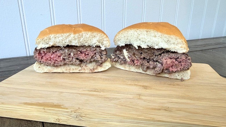 A close-up of a burger cut in half on a wooden cutting board, showing a center with pockets of pink and brown throughout