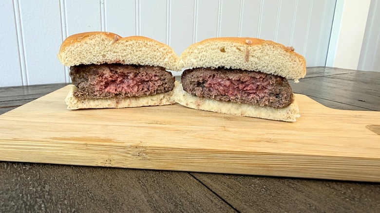 A close-up of a burger cut in half on a wooden cutting board, showing a super juicy and pink center