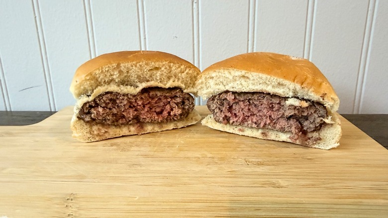 A close-up of a burger cut in half on a wooden cutting board, showing a pink center